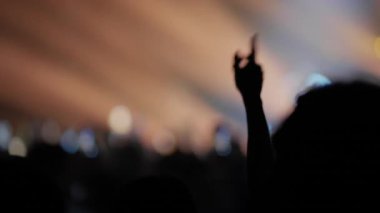 Silüetli bir kalabalık konserin tadını çıkarıyor. Bir vantilatör müziğe el sallarken, diğeri akıllı telefonuyla kayıt yapıyor. Sıcak, bulanık sahne ışıkları canlı, atmosferik bir arka plan yaratır..