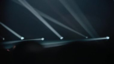 Dinamik beyaz sahne ışıkları canlı müzik konserinde siluetli kalabalığın üzerinde yanıp sönüyor. Seyirciler el ele tutuşarak festivalin enerjik atmosferini yakalıyorlar..