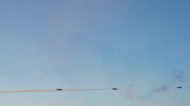 Birkaç akrobatik jet açık mavi gökyüzünde uçarak uzun kırmızı ve beyaz dumanlar bırakır. Uçaklar bir hava gösterisinde etkileyici bir gösteri yaparak çapraz manevra yapıyorlar..