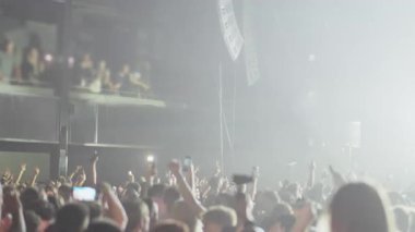 Büyük bir kalabalığın konserde ya da festivalde dans edişinin görüntüleri. Güçlü ışık demetleri üzerlerini silerken insanlar telefonları tutuyor ve dramatik bir karartma sahnesiyle sona eriyor..