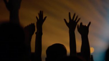 Bir müzik festivalinde enerjik bir kalabalığın siluetleri. İnsanlar sarı, mavi ve kırmızı renkli telefonlar eşliğinde ellerini ve filmlerini kaldırarak heyecan verici bir atmosfer yaratıyorlar..