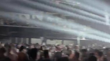Canlı müzik konserinde ya da çılgın bir partide büyük bir kalabalığın dinamik montajı. Güçlü beyaz ışıklar karanlık, puslu mekanı silip süpürerek enerjik ve heyecan verici bir atmosfer yaratıyor. Titrek pov çekimi.