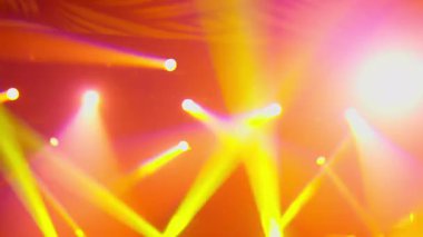 Bir konser salonunda ya da gece kulübünde yanıp sönen ve hareket eden sahne ışıkları. Puslu bir atmosferde açık mavi, kırmızı, turuncu ve mor renkli ışınlar. Canlı bir olay için enerjik ışıklandırma efektleri.