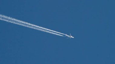 Yüksek irtifada, açık mavi bir gökyüzünde uçan bir yolcu uçağının uzun beyaz kontrastlar ya da buhar izleri bıraktığı video görüntüleri. Temiz, minimalist bir atış..