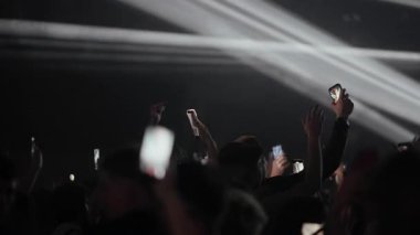İnsanlar telefonlarıyla kayıt yaparken, konser kalabalığının içinden bir video. Sahne karanlıktan yoğun kırmızı ışığa dönüşür, sonra parlak, coşkulu sahne ışığı gösterisine. Modern bir canlı olay deneyimi.