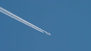 Yüksek irtifada uçan ticari bir yolcu uçağının uzun vadeli video görüntüleri. Jet, uçsuz bucaksız, berrak, derin mavi gökyüzünde uzun beyaz zıtlıklar bırakır..