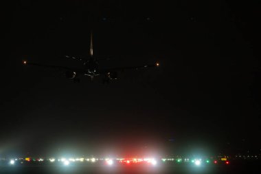 Yolcu uçağı gece vakti parlayan navigasyon ışıklarıyla havaalanı iniş pistine yaklaşıyor.