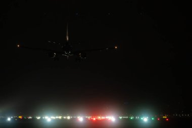 Uluslararası havaalanına gece uçuşu sırasında pist ışıklarına doğru inen ticari uçaklar.