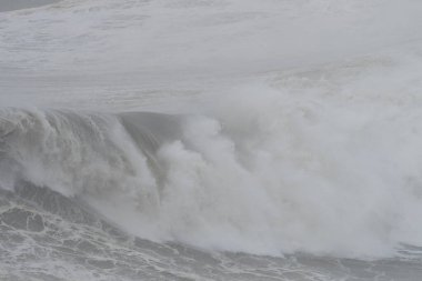 Dev bir gri dalganın kıvrımlarının detaylı görüntüsü ve fırtınalı bir denizde ağır beyaz spreyle kırılmaya başlıyor.