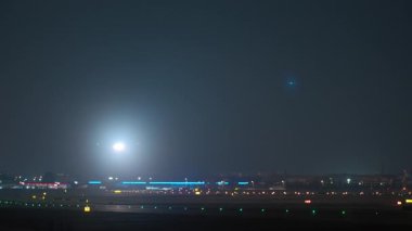 Parlak iniş ışıkları olan ticari bir uçak gece havaalanı pistine iniyor ve vergilendiriliyor.