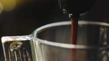 Temiz cam bardağa sıcak, taze espresso döken bir kahve makinesinin makro görüntüsü. Koyu, zengin kahve fincanı doldurur ve güzel bir krema oluşturur. Sıcak, samimi ve davetkar bir atmosfer.