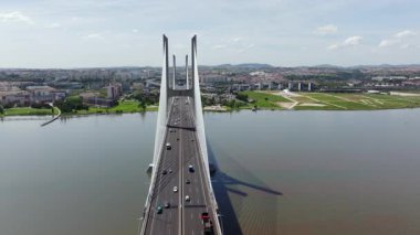 Portekiz, Lizbon 'daki görkemli Vasco da Gama Köprüsü' ne doğru uçan hava aracı görüntüleri. Parlak ve güneşli bir günde arabalar ve kamyonlar Tagus Nehri üzerindeki köprüden geçtiler. Şehir manzarası görünür.