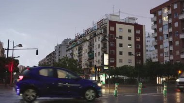 Yağmurlu bir akşamda şehir kavşağında araba trafiği. Islak asfalt, araçlar hareket bulanık ışık yolları oluştururken şehir ışıklarını yansıtır. Huysuz, atmosferik şehir hayatı