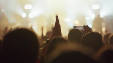 Heyecanlı bir seyircinin arkasından gece rock konserinde alkış ve tezahürat, parlak spot ışıkları ve dumanla aydınlatılmış.