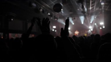 Siluetli bir kalabalığın, dinamik sahne ışıkları ve atmosferik bokeh efektlerine karşı alkış ve kutlama için el kaldırdığı enerjik canlı konser videosu