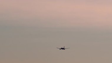 Bir yolcu uçağının silueti güzel bir pastel günbatımı gökyüzüne doğru uçuyor. Uçak iniş için yaklaşıyor, sıcak ve renkli ufka doğru uçarken küçülüyor. Huzurlu yolculuklar..
