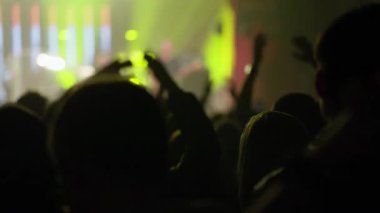 Canlı bir konser veya müzik festivalinde siluetli bir seyircinin dinamik videosu, el kaldırma ve coşkuyla tezahürat yapma, sahne ışıklarını yeşil, sarı ve kırmızı renkte değiştirme. Etkileyici olay deneyimi.