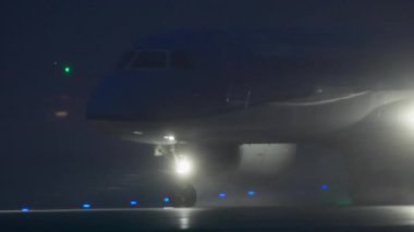 Islak bir havaalanı pistinde hızla hızlanan ticari bir jet uçağı, güçlü iniş ışıkları sisli su spreyini parlak bir şekilde aydınlatıyor. Dinamik hareket bulanıklığı hız ve verimliliği gösteriyor