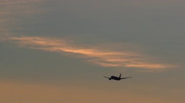 Bir ticari uçak, ılık turuncu ve serin mavi tonlarıyla güzel bir günbatımı gökyüzüne karşı siluetlenir.