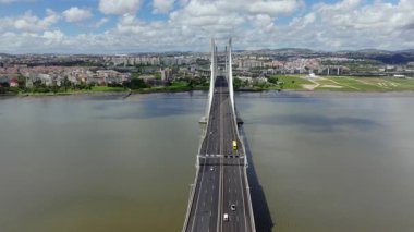 Portekiz, Lizbon 'daki Vasco da Gama Köprüsü boyunca ilerleyen çarpıcı hava aracı görüntüleri. Parlak, parçalı bulutlu bir günde Tagus Nehri 'nden şehre doğru akan trafiği gösterir.