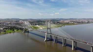 Portekiz, Lizbon 'daki ikonik Vasco da Gama Köprüsü üzerinde uçan hava aracı görüntülerini tarıyoruz. Güneşli bir günde şehir manzaralı Tagus Nehri 'ni geçerken trafiği gösterir.