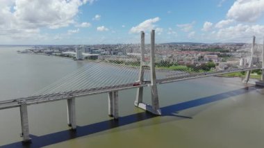 Hava aracı görüntüleri, Lizbon, Portekiz 'deki muhteşem Vasco da Gama Köprüsü' nü gözler önüne seriyor. Çekimde modern mühendislik, şehir trafiği ve mavi gökyüzünün altındaki geniş Tagus Nehri sergileniyor.