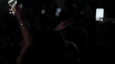 Canlı müzik konserinde ya da festivalde enerjik bir kalabalık, pek çok insan ellerini kaldırıyor ve gösteriyi akıllı telefonlarla kaydediyor. Parlak, yanıp sönen sahne ışıkları dansı aydınlatır.