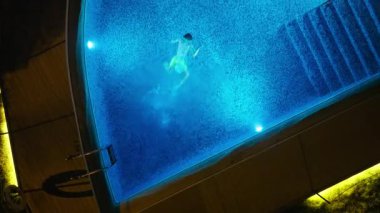 Hava aracı gece vakti güzelce aydınlatılmış mavi bir yüzme havuzunda zarif bir şekilde yüzen birini yakalar.