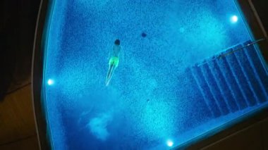 Hava aracının çektiği görüntülerde, gece vakti, göz kamaştırıcı, parlak, mavi bir yüzme havuzunda yüzen bir insan görülüyor. Sakin sahne yüzücü hareketini ve parlayan suyu vurguluyor.