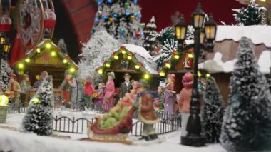 Çekici, animasyon bir Noel köyünün yakın çekimi. Karlı bir pazar sahnesinde yanan tezgahlar, dönme dolap ve şenlikli dekorasyonlarla figürler dolaşır.