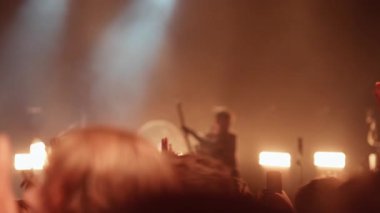 Canlı sahne ışıkları ve lazerler enerjik, dalgın bir atmosfer yaratırken, hareketli bir konser seyircisinin elleri havada ve telefon kayıtları kaydediliyor.