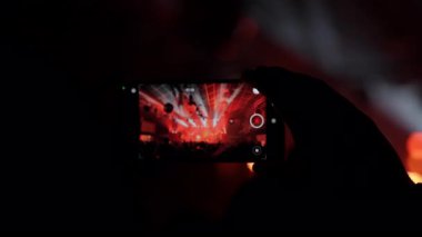 Zeka küpü bir silueti canlı bir konserde göz kamaştırıcı ışık gösterisini ve enerjik kalabalığı çekerken gösteren etkileyici bir bakış açısı videosu. Olay devamlılığını ve cep telefonunu tasvir etmek için mükemmel