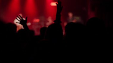 Enerjik konser kalabalığı tezahürat yapıyor, ellerini kaldırıyor ve canlı kırmızı, mavi ve mor sahne ışıkları gibi dans ediyor.