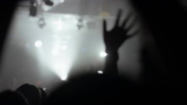 Canlı bir müzik konseri ya da etkinliğinde siluet içinde ellerini sallayan bir kalabalık. Parlak sahne ışıkları dumanlı bir atmosferi aydınlatarak enerjik ve heyecan verici bir parti havası yaratır.