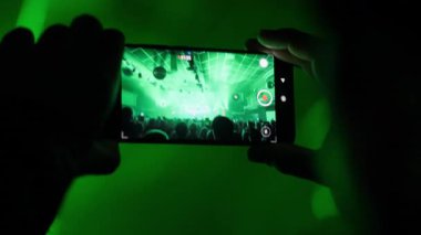 POV canlı bir konseri akıllı bir telefonla çekiyordu. Dinamik yeşil ve renkli ışıklar enerjik bir kalabalığı aydınlatır. Eğlence, etkinlik ve teknoloji temaları için mükemmel.