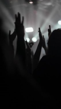 Siluetli kalabalık, dinamik sahne ışıkları altında ellerini kaldırdı. Bir konserin, ibadetin, festivalin veya kulübün enerjik ve duygusal atmosferini yakalar