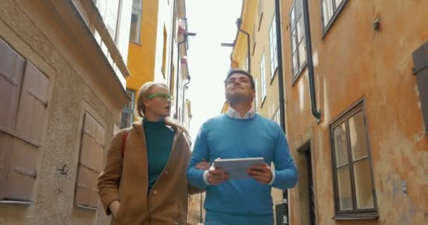 Young couple with pad walking in old narrow street — Stockvideo