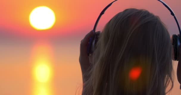 Menina ouvindo música e olhando para a cena do pôr do sol — Vídeo de Stock