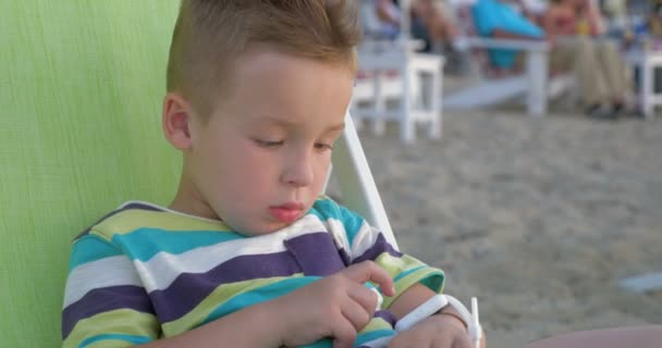 Маленький хлопчик з розумним годинником сидить у кріслі палуби — стокове відео