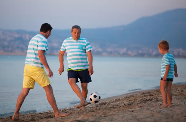Семейная команда из трех человек играет в футбол на берегу моря — стоковое фото