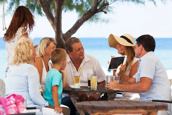 Family looking at photo on touch pad in outdoor cafe — Stock Photo, Image