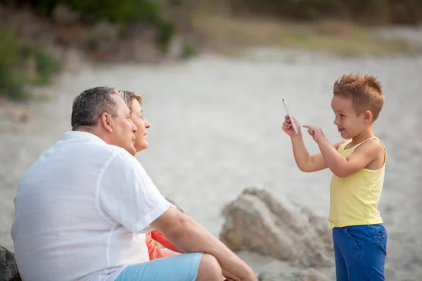 Boy taking phone photo of grandparents outdoor — Stock Photo, Image