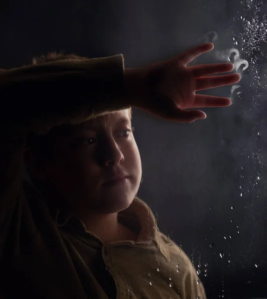 Niño mira por la ventana fuera de la lluvia ventana y una hoja cae — Foto de Stock