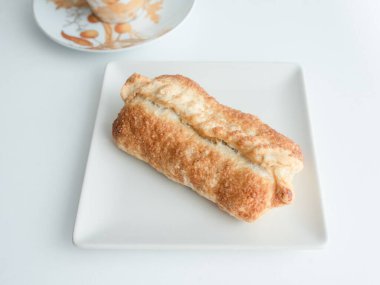 Yanında kahve fincanı olan beyaz bir tabağa taze pişmiş hamur işi.