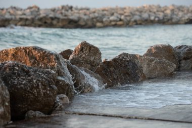 Kayalık kıyı manzarasında kayaların üzerinde hafif dalgalar, huzurlu bir ortam yaratıyor, doğa severler ve su kenarında dinlenmek isteyenler için mükemmel.