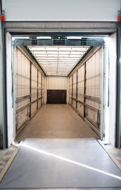 Boş yükleme alanı, parlak doğal ışığın boşluğu aydınlatmasına olanak sağlayan açık kapıları içerir.