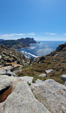 Kıyı manzarası, kayalık uçurumlar, yemyeşil yemyeşil ve parlak mavi bir gökyüzü altında parıldayan okyanus dalgaları, doğanın güzelliğinin sükunetini gösteriyor.