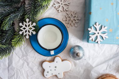 Mavi bir kupa, zencefilli kurabiye ve kar taneli süslemeler içeren kış temalı masa düzenlemesi, rahat bir atmosfer yaratıyor.