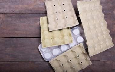 Çevreye duyarlı tüketiciler için sürdürülebilir paketleme seçeneklerini vurgulayan ahşap bir yüzeyde, geri dönüştürülmüş malzemelerden yapılmış farklı yumurta kutuları sergilenmektedir.