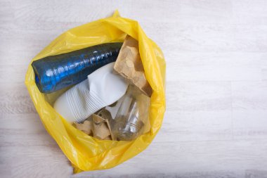 Sarı torba plastik şişeler, fincanlar ve karton gibi çeşitli geri dönüşümlü eşyalar içeriyor, uygun atık imhası ve çevresel sorumluluğun önemini vurguluyor